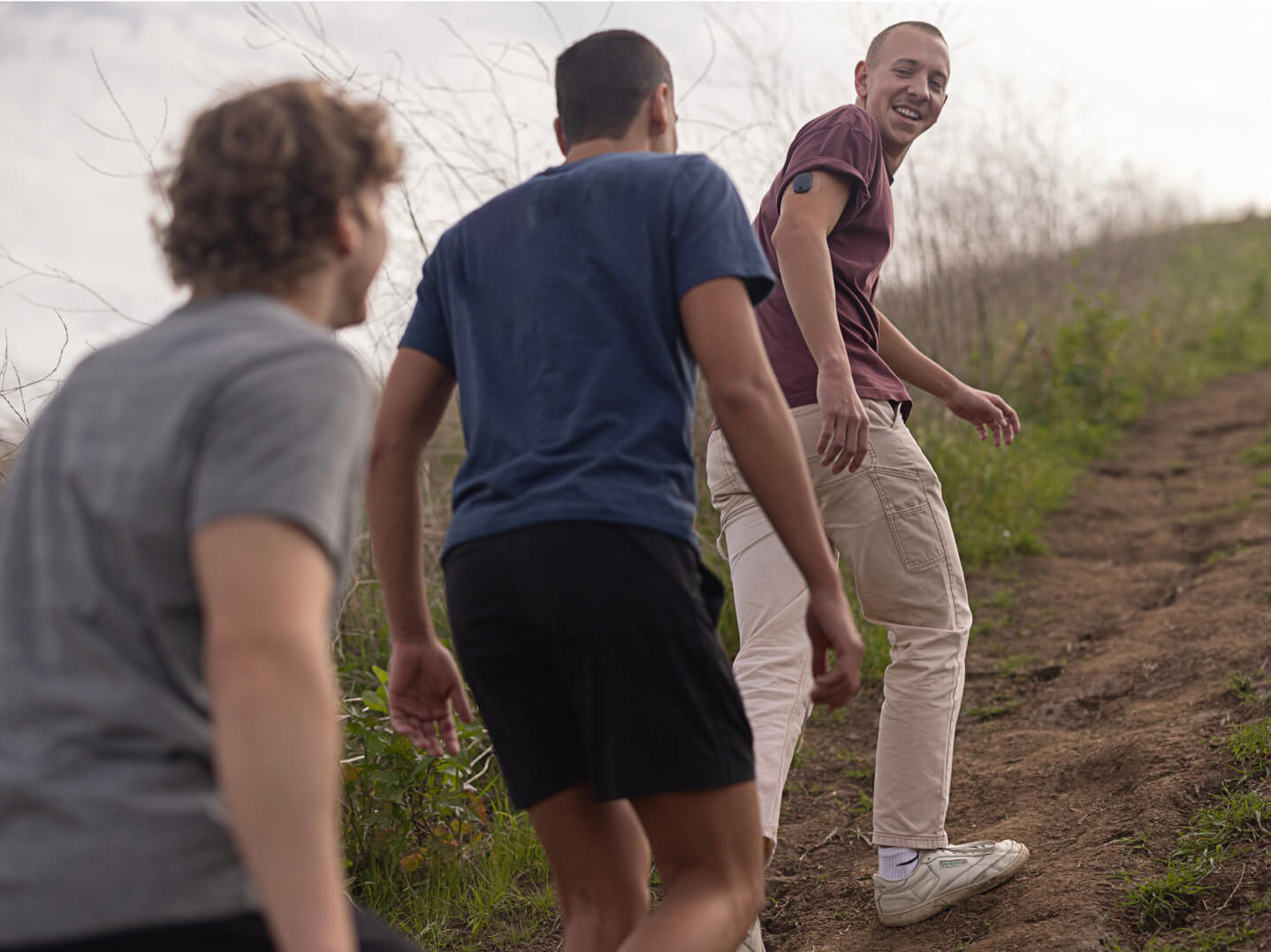 Three people are hiking up a dirt trail, smiling and looking back, one wearing the Eversense CGM
